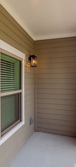 Botanic Luxury Apartments A screened-in balcony with brown siding, a light fixture, and a view of apartment buildings and a courtyard outside.