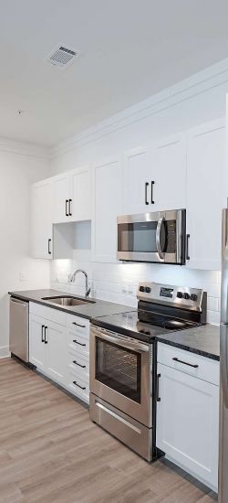 Botanic Luxury Apartments Modern kitchen with white cabinetry, stainless steel appliances, a wine rack, and wood flooring. Open hallway visible.