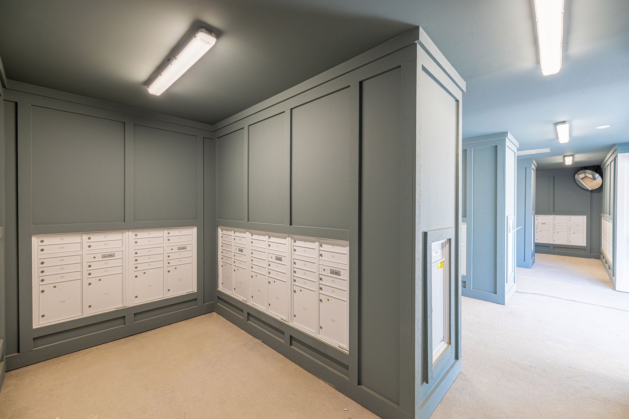 Botanic Luxury Apartments Interior hallway with rows of white mailboxes set into sleek gray walls and ceiling lights illuminating the space.