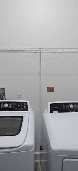 Botanic Luxury Apartments A laundry room with a white washing machine on the left and a white dryer on the right, and a wire shelf above.