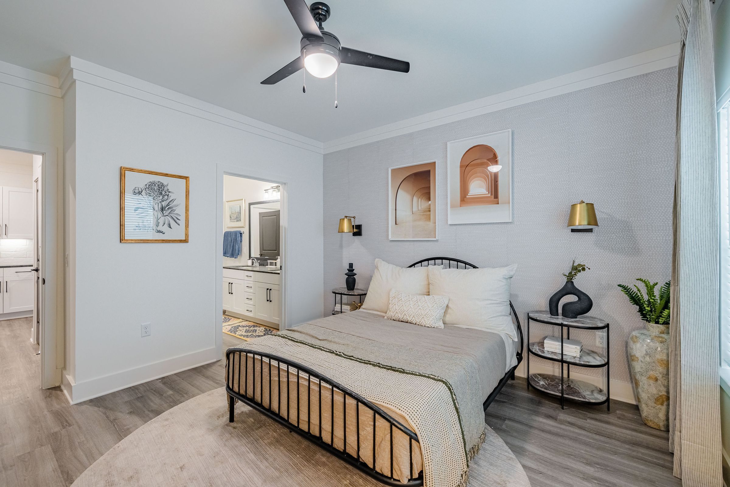 Botanic Luxury Apartments Modern bedroom with a metal bed frame, neutral bedding, decorative wall art, ceiling fan, and en-suite bathroom.